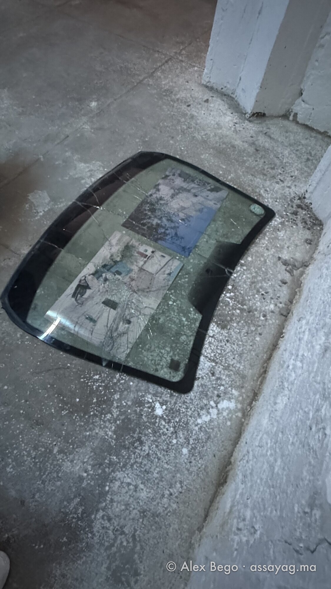 Une photographie posée sous un pare-brise éclaté, à même le sol de l’exposition